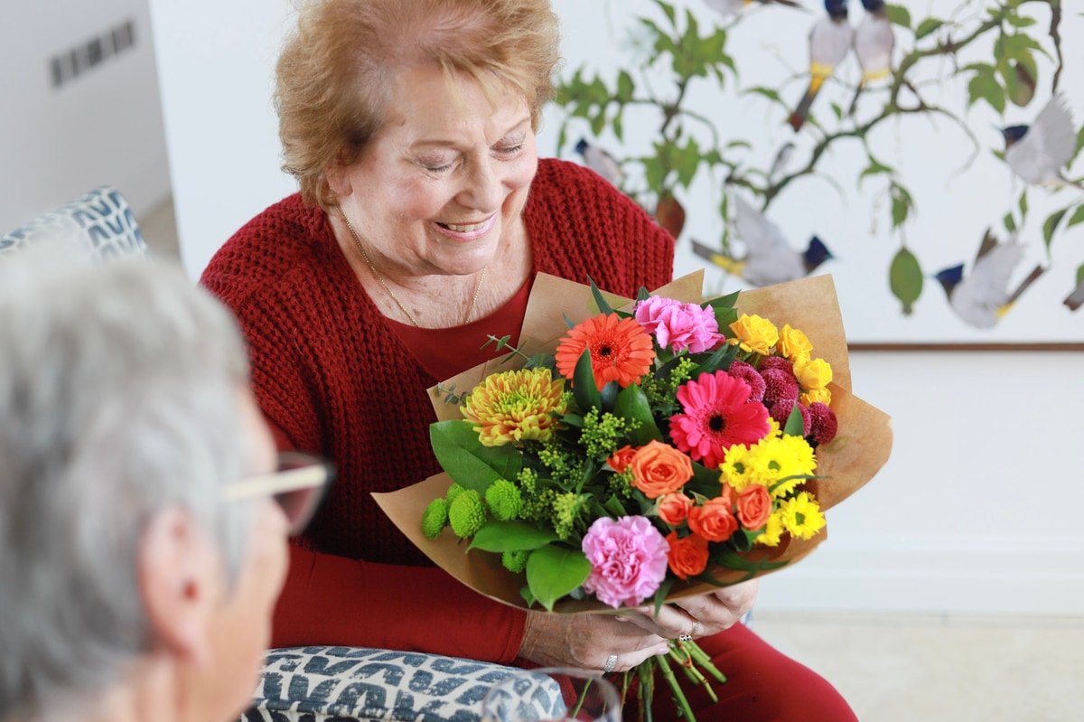 .Woman sitting with friend enjoying flowers delivered same day